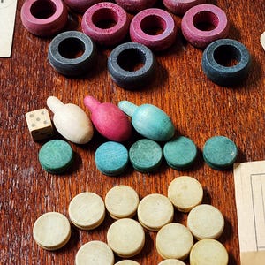May include: A wooden game board with red, black, and green game pieces. There are also white, red, and blue game pieces shaped like bowling pins. The game board is made of wood and has a dark brown finish.