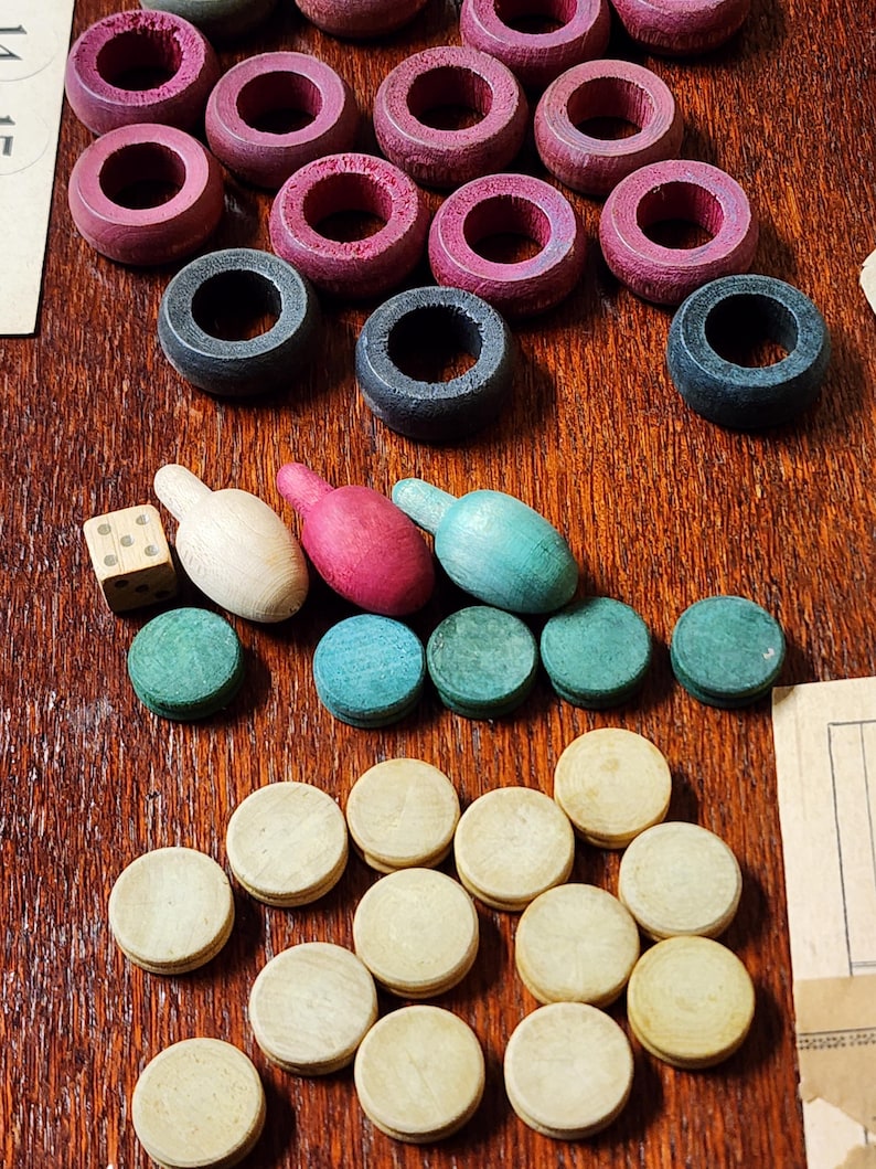 May include: A wooden game board with red, black, and green game pieces. There are also white, red, and blue game pieces shaped like bowling pins. The game board is made of wood and has a dark brown finish.