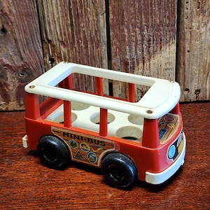 May include: A vintage red and white toy bus with black wheels. The bus has the words "MINI-BUS" printed on the side, along with various symbols. The bus has a white roof and a series of holes inside.