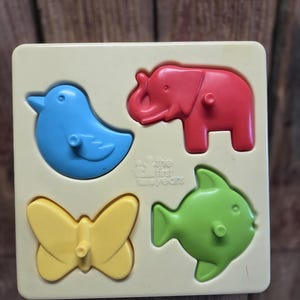 May include: A children's toy featuring a light yellow base with four colorful animal shapes: a blue bird, a red elephant, a yellow butterfly, and a green fish. The toy is designed for early childhood development.