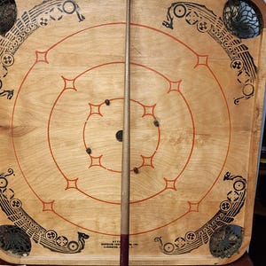 May include: A vintage wooden game board with a circular playing area and a wooden cue stick. The board features a Viking ship design and a net in the corner. The game board is surrounded by a set of colorful wooden rings.