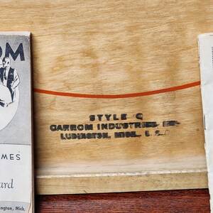 May include: Close-up of a wooden game board with the text "STYLE C CARROM INDUSTRIES INC. LUDINGTON, MICH. U.S.A." printed on it.