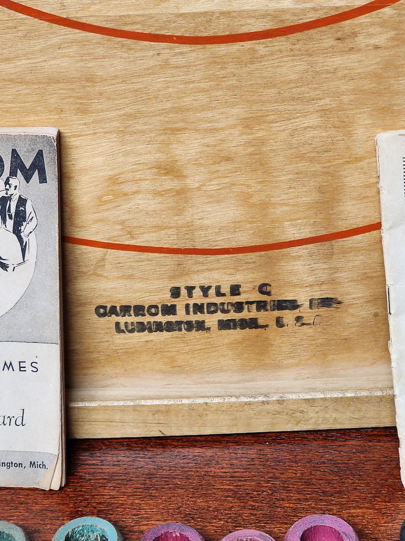 May include: Close-up of a wooden game board with the text "STYLE C CARROM INDUSTRIES INC. LUDINGTON, MICH. U.S.A." printed on it.