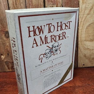 May include: A white box game titled "How to Host a Murder" with maroon text and accents. The box features the text "So Much Fun, It's Almost Criminal!" and "A Matter of Faxe". Two theatrical masks are also displayed.