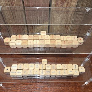 May include: Wooden word dice arranged on clear acrylic shelves. The dice are engraved with various words and symbols, including "THEM", "WORD", and "★". The arrangement suggests a game or educational tool.