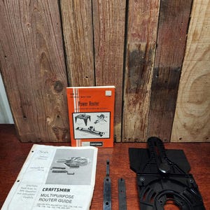 May include: An assortment of Craftsman power router tools and manuals. The image includes a black router base, metal parts, and two manuals: "Power Router" and "Craftsman Multipurpose Router Guide". The background is a wooden surface.