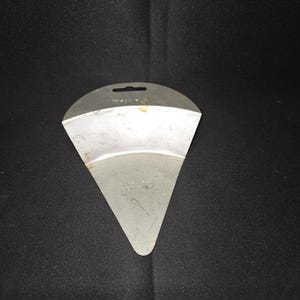 May include: A silver-colored, metal spatula with a triangular shape and a curved top. The spatula has a small hole at the top for hanging. The surface shows some wear and tear.