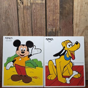 May include: Two vintage Playskool puzzles featuring Disney characters. One puzzle shows Mickey Mouse in an orange shirt and red pants. The other puzzle shows Pluto with a bone. Both puzzles are on a wooden background.