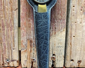 May include: A vintage bottle opener with a dark blue leather handle and a circular top. The top features the text "Monmouth Tartan Club 74" in a circular design. The opener has a gold-colored metal accent.