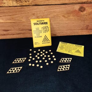 May include: A yellow box with the words "Magnetic Solitaire" and "Glows in the Dark!" printed on it. The box contains a game with wooden pieces and a game board. The game is for ages 6 and up.