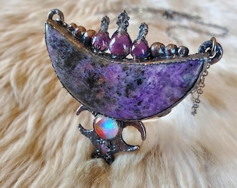 May include: A handcrafted necklace featuring a crescent-shaped pendant with a vibrant purple stone. The pendant is adorned with small purple gems and a colorful opal-like stone. The necklace has a silver chain and a unique, artistic design.