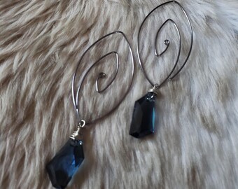 May include: A pair of earrings featuring dark blue, faceted, teardrop-shaped crystals suspended from thin, silver-toned wire frames. The wire is shaped into an elongated, open spiral design, with the crystal charms attached at the base by wire wrapping.