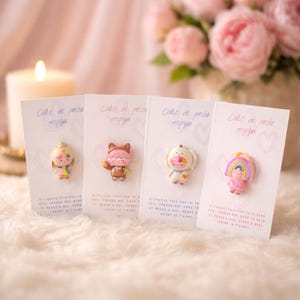 May include: Four small, colorful figurines on cards with French text. Each figurine has a unique design, including a princess, a cat, a dog, and a rainbow. The cards have a heart design and the text "Calin de poche magique".