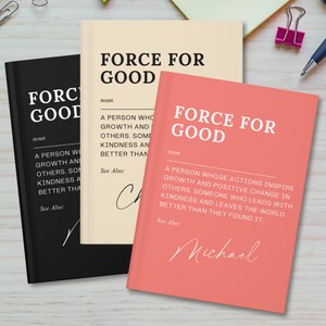 Puede incluir: Tres cuadernos negros y blancos con el texto "Force for Good" en la portada. Los cuadernos tienen una definición del término "Force for Good" y un espacio para una firma. Los cuadernos están sobre una superficie de madera clara.