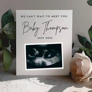 May include: A gray card with the text "We can't wait to meet you Baby Thompson May 2025" and a black and white ultrasound image.