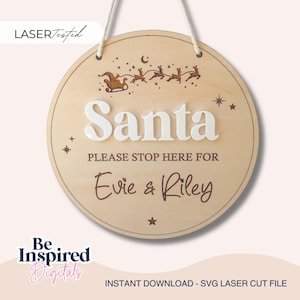 Op de afbeelding: Een rond houten hangbord met een lasergegraveerd ontwerp van de kerstman in een slee met rendieren. Het woord Santa staat in verhoogde witte letters, gevolgd door de tekst PLEASE STOP HERE FOR Evie & Riley in donkerbruin schrift.