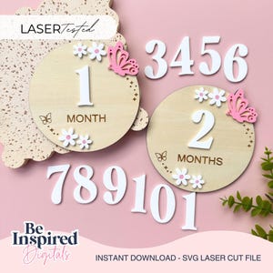Può includere: Segnalini mensili in legno con numeri bianchi, fiori e farfalle rosa. Il set include segnalini per 1 e 2 mesi, più numeri individuali. Il testo "LASER Tested" e "Be Inspired Digitals" sono visibili.