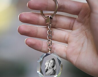 May include: A clear crystal keychain with a faceted, spherical pendant. Inside the pendant is a black and white image of a person holding a cat. The keychain has a silver-colored metal ring and chain.
