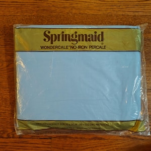 May include: A blue fitted sheet packaged in plastic. The packaging has a gold label with the text "Springmaid Wondercale No-Iron Percale" and the text "Twin Fitted Sheet for 39 x 76 in. (99 x 193 cm.) Mattress 60% Polyester 40% Cotton/Cotton".