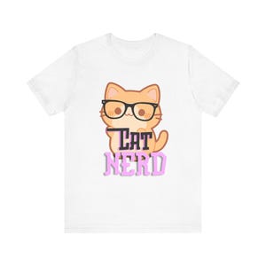 以下が含まれることがあります： 白いTシャツに、眼鏡をかけたオレンジ色の猫の漫画と、ピンク色の「Cat Nerd」という文字が書かれています。