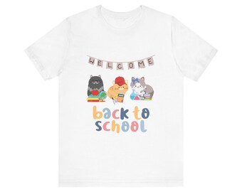 May include: White t-shirt with a colorful graphic of three cats holding school supplies and a banner that says "WELCOME BACK TO SCHOOL".