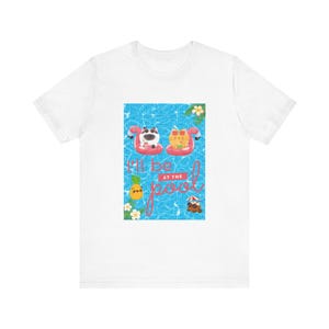 May include: White t-shirt featuring a graphic of two cats on pink flamingo inflatables in a blue swimming pool. The text "I'll be at the pool" is written in pink on the graphic.