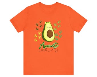 May include: Orange t-shirt with a green avocado illustration and the text "Avocoato" in green cursive lettering. The avocado has a cute face and is surrounded by green paw prints.
