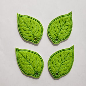 May include: Four green felt leaf-shaped keyrings with a green stitched outline and a small green button in the centre of each leaf.