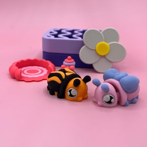 Puede incluir: Una colección de gomas de borrar y artículos decorativos coloridos y caprichosos. Incluye una goma de borrar con forma de abeja con rayas negras y amarillas, una goma de borrar con forma de caracol rosa y azul, una goma de borrar con forma de flor y un artículo rosa en forma de anillo.