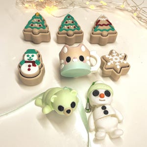 Peut inclure: Divers ornements de Noël, dont des formes de sapin, de bonhomme de neige et d'étoile en pain d'épices. Un ours polaire vert clair et un bonhomme de neige blanc sont également présents. Une tasse en forme de chat est également incluse.
