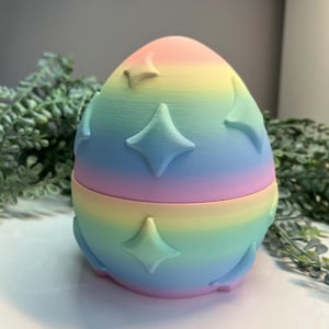 Könnte beinhalten: Ein pastellfarbener, eiförmiger Behälter in Regenbogenfarben mit einem erhabenen Diamantenmuster. Der Behälter ist aus Kunststoff und besteht aus zwei Teilen.