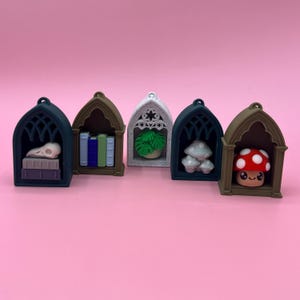 以下が含まれることがあります： さまざまな色の5つのミニチュアゴシックアーチで、それぞれに異なるオブジェクトが含まれています。アイテムには、頭蓋骨、本、鉢植えの植物、キノコ、赤い帽子と白い水玉模様のキノコが含まれます。背景は無地のピンクです。