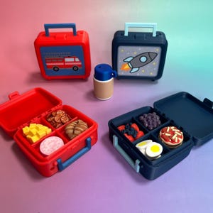 May include: Two rectangular lunch boxes with handles, one red and one dark blue, featuring a fire truck and a rocket ship graphic. Inside are miniature food items like cheese, crackers, fruit, and pizza. A small blue and tan thermos sits between them.