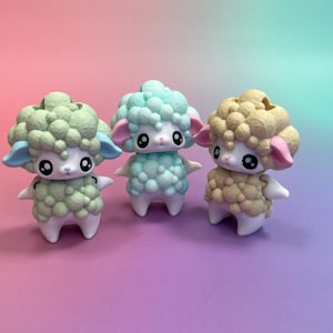 May include: Three colourful sheep figurines. One is green with blue accents, another is light blue, and the third is tan. Each has a fluffy, textured coat, pink ears, and large, black eyes. They stand on white legs.