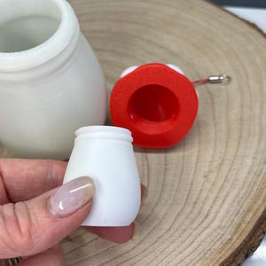 Może przedstawiać: Dwa białe plastikowe pojemniki z czerwoną pokrywką. Pokrywka ma małe białe k&oacute;łko na g&oacute;rze. Pojemniki są r&oacute;żnych rozmiar&oacute;w. Większy pojemnik jest wyższy i szerszy od mniejszego.