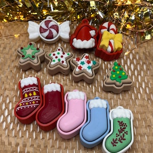 Puede incluir: Una colección de adornos navideños de varias formas y colores. Incluye un caramelo, un gorro de Papá Noel, estrellas de jengibre, un árbol de Navidad y varios calcetines navideños en rojo, rosa, azul y verde.