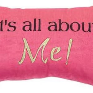 May include: Pink pillow with black and white polka dot trim. The pillow has the text "It's all about Me!" embroidered on it in black and gold thread.
