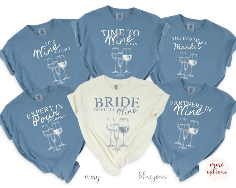 May include: Six blue jean and ivory t-shirts with wine-themed text and graphics. The shirts feature text such as "It's Wine O'Clock", "Time to Wine Down", "You Had Me at Merlot", "Expert in Pour Decisions", "Bride on Cloud Wine", and "Partners in Wine".