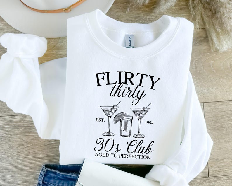 May include: White sweatshirt with black text that reads "Flirty thirty est. 1994 30's Club aged to perfection" and a graphic of three martini glasses with olives.