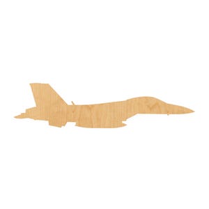 May include: A flat, laser-cut wooden cutout in the shape of a fighter jet aircraft. The object features a natural light brown wood grain texture and a distinct silhouette showing the wings, fuselage, and tail fin of a military jet plane.