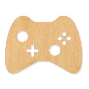 May include: A flat, light-colored wooden cutout shaped like a video game controller. The surface features a natural wood grain pattern and includes cutouts for two circular analog sticks, a directional pad, and four smaller circular button holes.