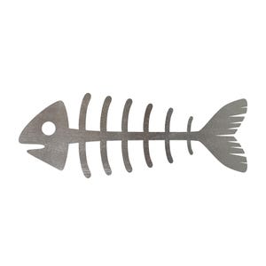 May include: A silver-colored fish skeleton cutout. The design features a fish head with an eye and mouth, a series of vertical ribs, and a detailed tail. The cutout is likely made of metal and is suitable for decorative purposes.