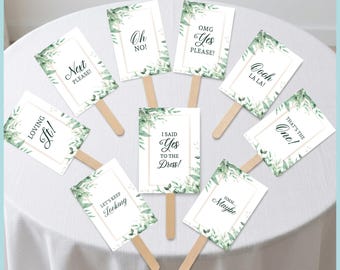 May include: A set of eight rectangular wedding dress shopping signs on wooden sticks, featuring white backgrounds with green watercolor leaf borders and gold frames. Each sign displays black text including phrases like Oh No, Yes Please, and I Said Yes.