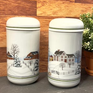 Peut inclure: Deux salières et poivrières en céramique blanche avec une bordure verte. Les salières présentent une scène d'hiver avec une ferme blanche, des arbres et un paysage enneigé.
