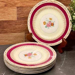 May include: Set of six vintage floral dessert plates with a cream colored center and a burgundy rim with gold accents. The plates feature a floral design with pink, yellow, and green flowers.