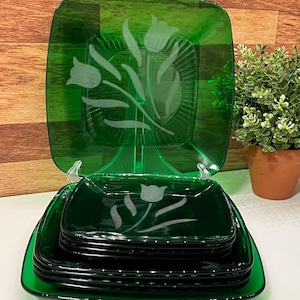 Può includere: Un set di piatti quadrati in vetro verde con un design a tulipano. Il set include un grande piatto da portata e diversi piatti più piccoli, tutti in un vivace colore verde. Il design del tulipano è inciso nel vetro.