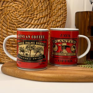 Könnte beinhalten: Zwei rote Kaffeetassen mit weißen Griffen und schwarzem Rand. Auf einer Tasse steht "Kenyan Coffee, Three Palms Brand, Strong & Sweet". Auf der anderen Tasse steht "Java Planter, Strong Blend Coffee."
