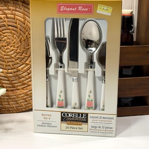 Peut inclure: Un ensemble de couverts en acier inoxydable de 20 pièces en boîte. L'ensemble comprend des fourchettes, des couteaux et des cuillères avec des manches blancs décorés de roses roses et de feuilles vertes. La boîte indique "Elegant Rose" et "Corelle Coordinates".