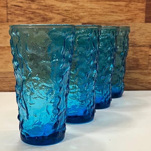 Peut inclure: Quatre grands verres bleus texturés. Les verres présentent un motif organique unique et une couleur bleu profond qui s'estompe vers une teinte plus claire vers le haut. Les verres sont disposés en rangée, mettant en valeur leur design.