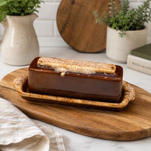 Pode incluir: Uma manteigueira retangular de cerâmica com um esmalte castanho escuro brilhante e uma borda texturizada em castanho claro. A tampa apresenta uma superfície superior distinta, salpicada de bege e castanho. A base é retangular e a condizer.